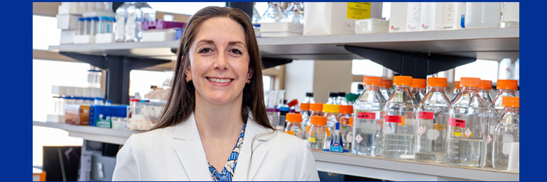 A researcher in a white lab coat standing in a laboratory at NEOMED.