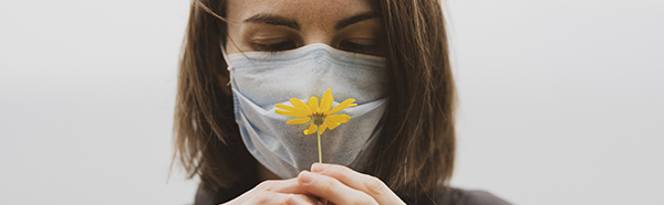 woman smelling flower while wearing a face covering