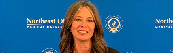 Amy Acton stands in front of blue NEOMED backdrop