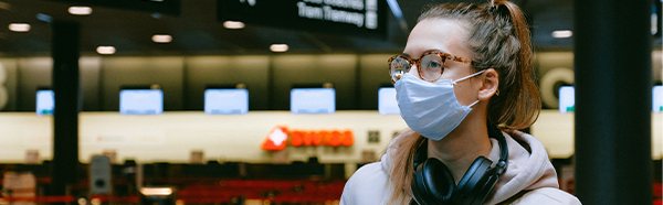 emale in airport wearing face covering with headphones around neck