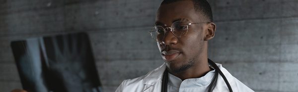 Male in white coat with stethoscope around neck holding an x-ray