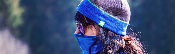 Woman wearing beanie, sunglasses and neck gaiter.