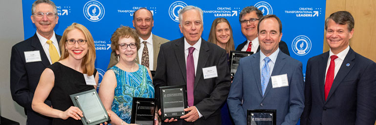 Nine people, many holding plaques, stand for a photo.