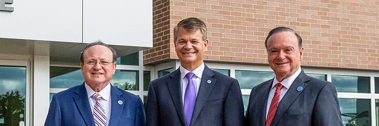 Three men standing in front of the front door of NEOMED.