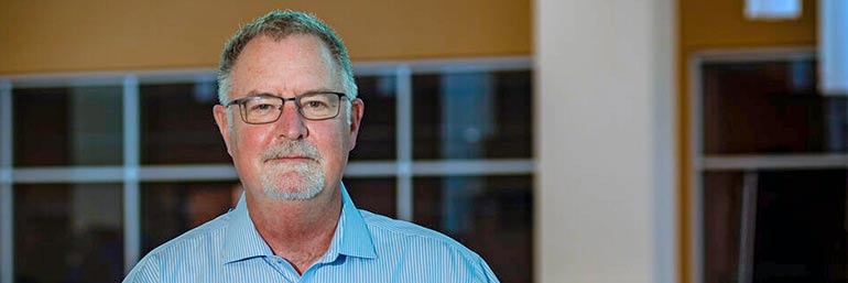 A man in a blue shirt stands in an atrium at NEOMED.