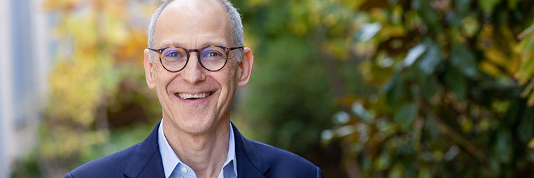 Ezekiel Emanuel smiles while standing in a garden on a fall day.