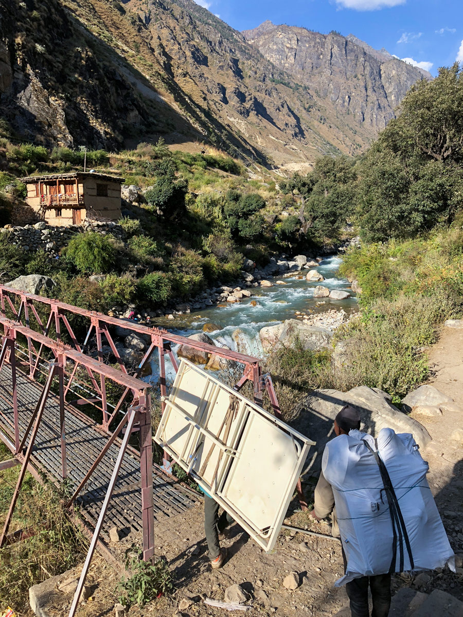 Two people carry supplies over a fast-moving river.