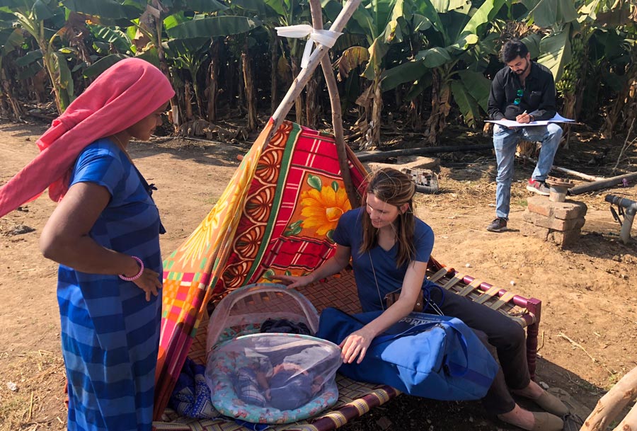 A student physician checks on a newborn in a field with crops in the background.